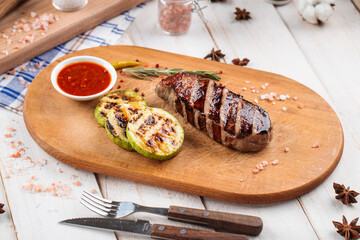 Grilled beef steak with squash slices and red sauce on the wooden board