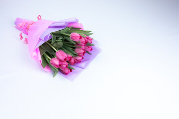 bouquet of festive spring tulips packed in a pink wrapper lie on a white table