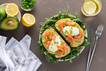 Delicious hearty breakfast, sandwiches with avocado paste, salmon and mozzarella on a plate with arugula and pea sprouts