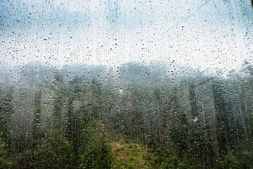Raindrops on glass window of cableway. Sad view from overhead cable Car