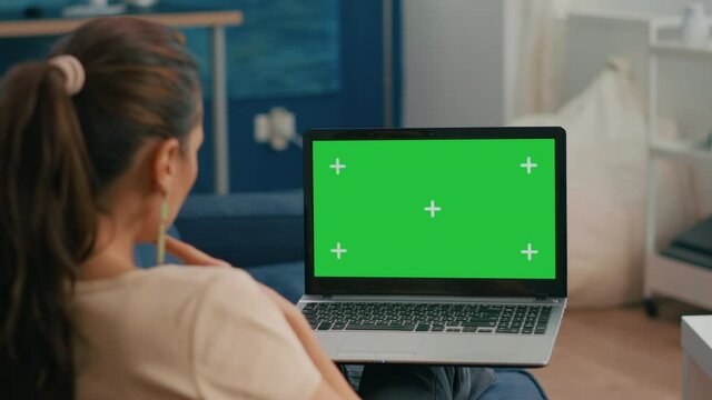 Caucasian female lying on sofa looking at laptop computer with mock up green screen chroma key display. Business woman working on financial graphs using isolated pc in home office
