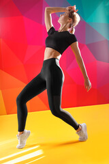 Full length image of a woman dressed in tight black sportswear, posing in studio, isolated yellow colorful background.