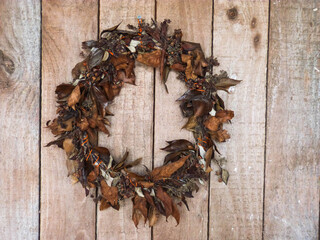 wreath made from brown dryed leaves on wooden front door in autumn