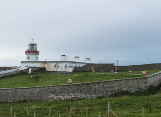 Fototapeta na wymiar white lighthouse with green grass and rocks in ireland landscape