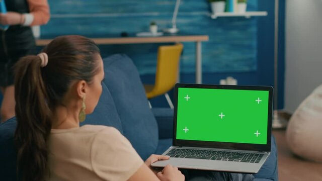 Freelancer sitting on couch working on business ideas using laptop computer with mock up green screen chroma key display. Caucasian female searching the network use isolated pc