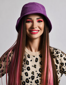 Happy active young woman with colored hair in stylish purple bucket hat and leopard pullover stands looking at camera over white background. Hair coloring, headdress concept