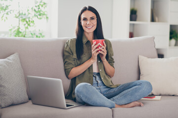 Full length photo of young cheerful woman happy positive smile sit couch home break pause enjoy hot coffee laptop