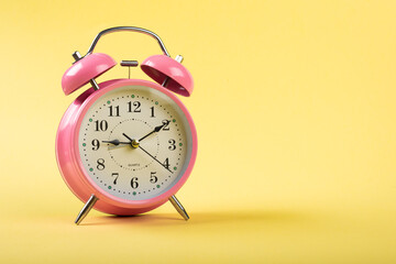 Pink color Table clock with a yellow background flat lay shot
