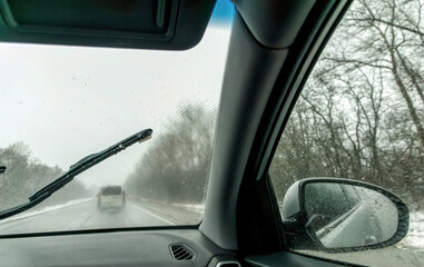 Naklejka premium Car wipers wiping the windshield. Winter highway during snowfall