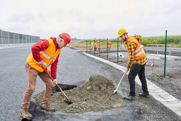 Zwei Bauarbeiter schaufeln Beton beim Straßenbau