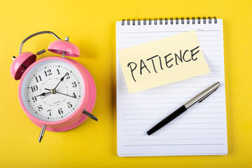  A table clock with Patience words Written on a sticky note with notepad and other elements on a Yellow background.