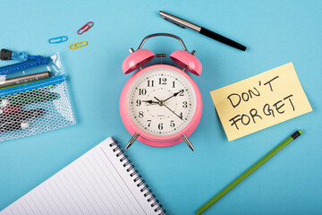  A table clock with words Dont forget Written on a yellow sticky note and Pen with other elements on a blue background