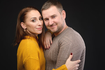 Caucasian married couple man and woman in an embrace on a black background. Casual style and bright clothes of an ordinary 30-year-old couple