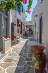 Fototapeta na wymiar Cycladitic alley with a narrow street and an exterior of a traditional whitewashed cafe with chairs and tables in Chora kythnos,cyclades, Greece.