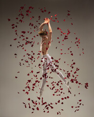 Loving. Young and graceful ballet dancer on studio background in flight, jump with rose petals. Art, motion, action, flexibility, inspiration concept. Flexible caucasian ballet dancer, moves in glow.