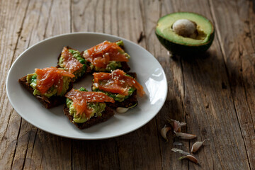Homemade toast on brown dark wooden rustic background. Open sandwich with dark rye bread, avocado and salmon. top view, free space. Healthy protein food, breakfast, lunch concept. Gourmet snack