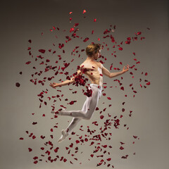 Obraz na płótnie Canvas Romance. Young and graceful ballet dancer on studio background in flight, jump with rose petals. Art, motion, action, flexibility, inspiration concept. Flexible caucasian ballet dancer, moves in glow.