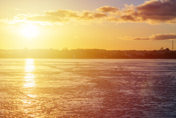 Winter landscape with frozen lake at sunrise or sunset. Lake glistening ice reflect a sun.Forest in the background.