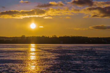 Naklejka premium Winter landscape with frozen lake at sunrise or sunset. Lake glistening ice reflect a sun.Forest in the background.
