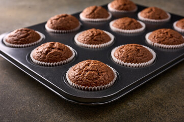 Homemade chocolate cupcakes in baking form on wooden background, selective focus, close up