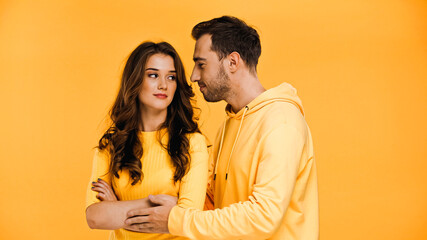 man calming curly girlfriend isolated on yellow