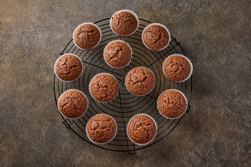 Homemade chocolate cupcakes on a grille stand on wooden background, top view
