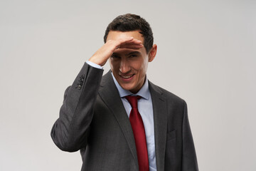 A cheap car in a classic suit and tie holds a hand near the face and smiles 