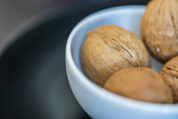 Heap, pile of whole walnuts in a round-shaped brown shell lie in a small white platter on black table on blurred bokeh backdrop. Macro