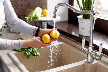 Close-up of a girl s hands washing a lemon in the sink in a home kitchen. The concept of health and...