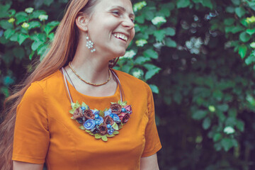 Laughing lovely young woman wearing a decorative floral necklace is looking away. Close-up portrait of a natural girl without makeup with tilted the head over a green background. Spring is coming.