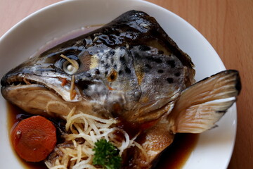 Braised salmon head with soy sauce or Salmon kabutoni on white round dish in close up view.