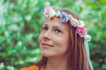 Smiling, dreaming pretty young woman wearing a decorative floral wreath is looking up away. Close-up portrait of a natural girl without makeup over a green background. Spring is coming.