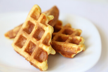 Belgian waffles in white plate. Healthy breakfast close up, pieces of freshly baked classic wafer