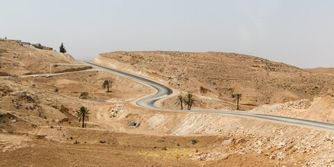 Brown and yellow desert sand with hills, road and palm trees, Tunisia, Africa