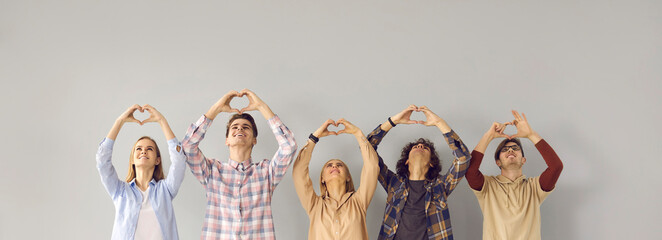 Group of happy grateful people looking up and doing symbolic heart shape hand sign gesture on gray...
