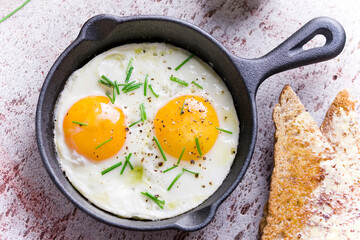 fried eggs with chives in an iron pan on a wooden table