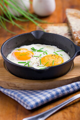 fried eggs with chives in an iron pan on a wooden table