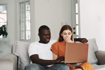  happy woman is sitting next to a man of African appearance near an open laptop