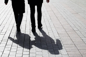 Couple walking down the street, silhouettes and shadows of two people on pedestrian sidewalk. Male and female legs, concept of relationships, city life, dramatic stories
