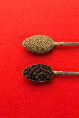 Black peppercorn and grinded pepper in spoons on red 