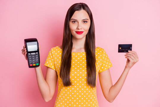 Photo of attractive serious young woman hold card reader debit card wear yellow dotted t-shirt isolated on pink color background