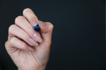 Female hand holding blue whiteboard marker on a black background