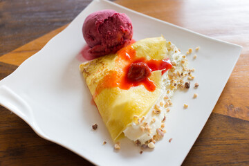 The fresh cream crepe on top with almond and strawberry sauce was served with forest berries sorbet ice cream and put on a white plate.
