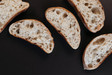 Sliced ciabatta bread on black background. Italian white bread. Top view.