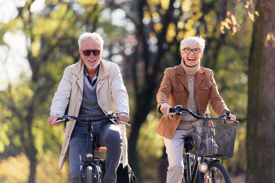 Cheerful Active Senior Couple With Bicycle In Public Park Together Having Fun. Perfect Activities For Elderly People. Happy Mature Couple Riding Bicycles In Park