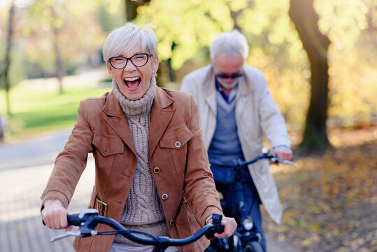 Cheerful Active Senior Couple With Bicycle In Public Park Together Having Fun. Perfect Activities For Elderly People. Happy Mature Couple Riding Bicycles In Park