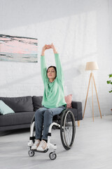 Brunette woman stretching arms while sitting in wheelchair at home