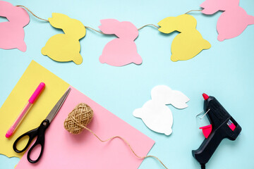 Easter decoration, diy: how to make a bunny garland using colored paper, bunny pattern, pen, rope, scissors. Final result and necessary materials.