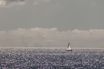 sailboat sails on the open sea under full sail with a sky full of clouds in the background and silver reflections on the sea