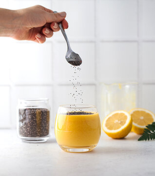 A woman decorates a yellow fruit smoothie with chia seeds. Healthy food, detox.